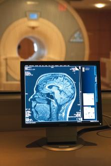 MRI scanner in background, image of human brain in the foreground