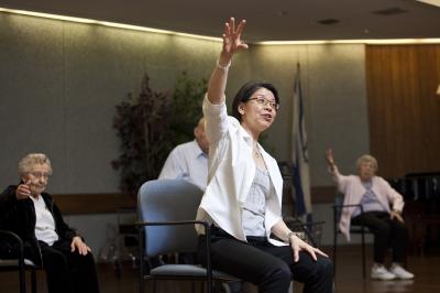 Exercise professional leading a group of elderly adults through chair exercises. 